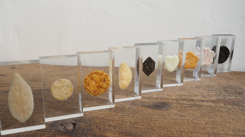 展示会用に制作したおせんべいのレジン封入サンプル10種類。透明レジンの中に、形や色の異なるおせんべいが美しく並べられています。