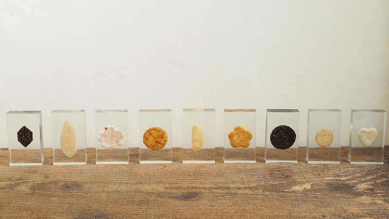 展示会用に制作したおせんべいのレジン封入サンプル10種類。透明レジンの中に、形や色の異なるおせんべいが美しく並べられています。